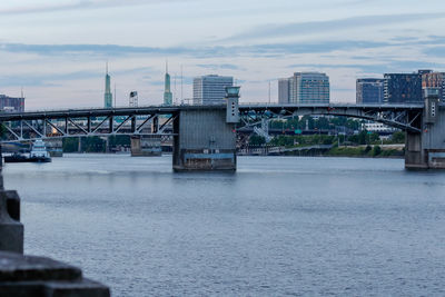 Bridge over river by buildings against sky