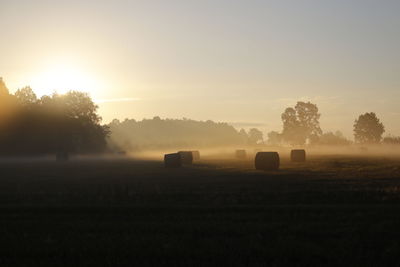 Hay bales on field against sky during sunset