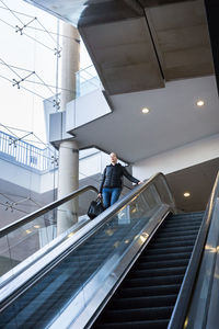 Low angle view of businesswoman standing on escalator at mall