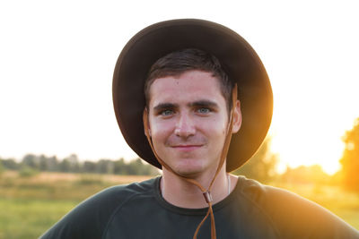 Young man farmer in cowboy hat at agricultural field on sunset with sun flare. closeup portrait 