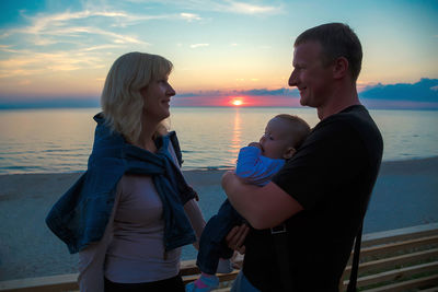 Friends at sea shore against sky during sunset