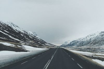 Street amidst snow covered mountains against cloudy sky