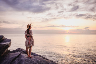 Rear view of woman standing on rock by sea against sky