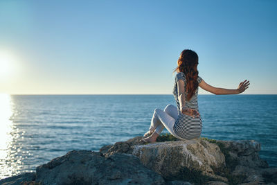 Woman sitting on rock by sea against clear sky