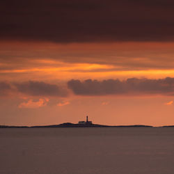 Silhouette of lighthouse on sea during sunset
