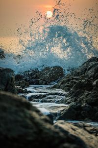 Waves splashing on rocks at shore against sky