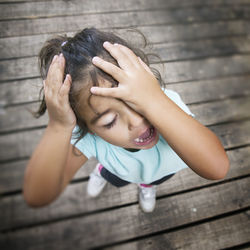 High angle view of girl with head in hands standing on boardwalk