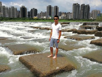 Portrait of young man wearing sunglasses standing on rock in river