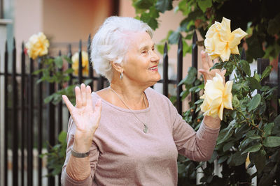 Elderly woman admiring beautiful bushes with yellow roses