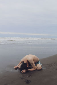 Man lying on shore at beach against sky