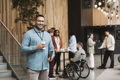 Portrait of happy male delegate holding disposable cup during coffee break at convention center