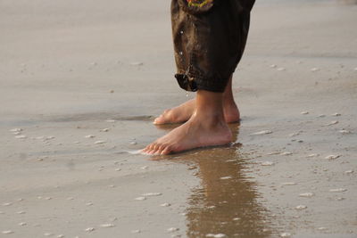 Low section of man walking on wet beach