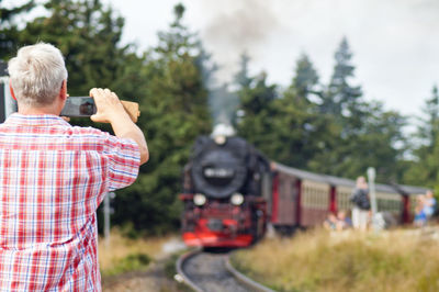 Rear view of man photographing steam train against sky