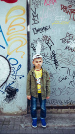Full length of boy standing against graffiti wall
