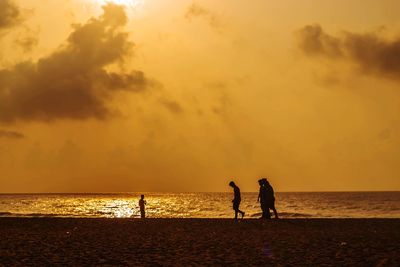 Silhouette people on beach against sky during sunset