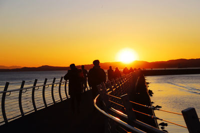 Silhouette people walking on pier against sea during sunset