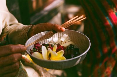 Close-up of hands holding flowers in bowl and incenses