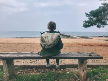 Rear view of man sitting on bench at beach