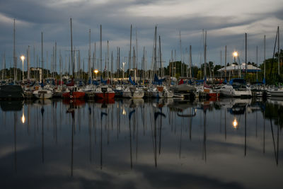 Sailboats moored at harbor against sky at dusk