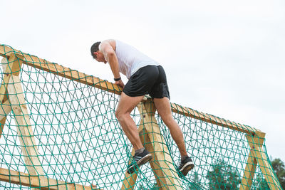 Low angle view of man standing by fence against sky