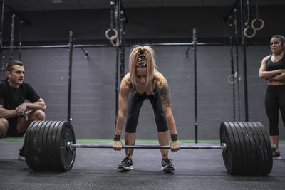 Athletes watching woman picking barbell while standing in gym