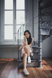 Portrait of smiling young woman sitting on spiral staircase at home