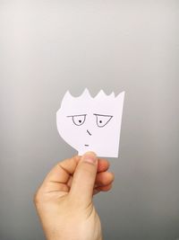 Close-up of hand holding paper with face drawn on it
