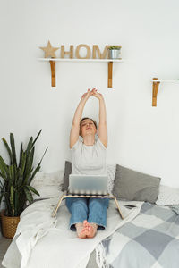 Portrait of woman using digital tablet while sitting on bed at home