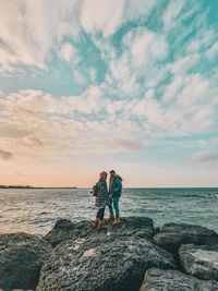 Men standing on rock by sea against sky