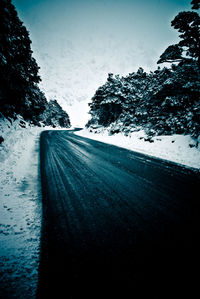 Snow covered road by trees against sky