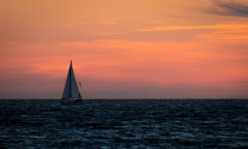 Sailboat sailing on sea against orange sky