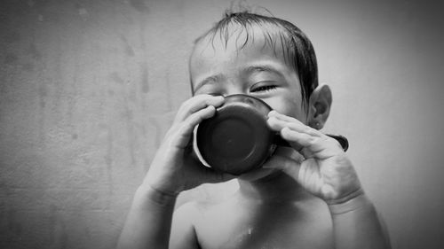 Portrait of cute boy drinking glass against wall