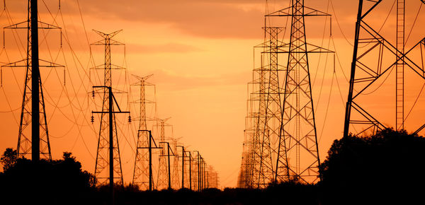 Silhouette electricity pylons against orange sky