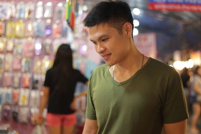 Smiling young man looking down while standing in market at night