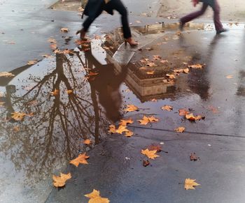 Low section of people standing on wet puddle during autumn