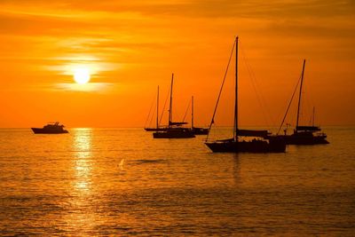 Silhouette sailboats on sea against dramatic sky during sunset