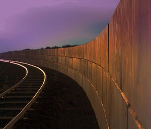 Railroad track by surrounding wall against sky during sky during sunset