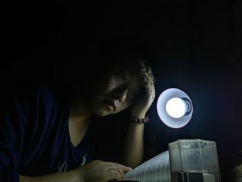 Young woman with head in hands reading book by electric lamp at home