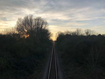 Railroad tracks amidst trees against sky during sunset