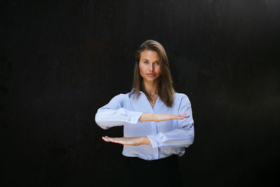 Portrait of smiling young woman gesturing equal sign while standing against black background
