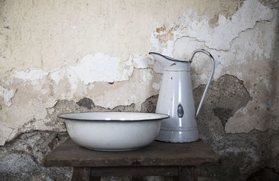 Close-up of old wash basin and water jar against wall at home