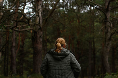 Back view of a young blonde woman hiking in forest. hiking woman walking in gloomy mystical forest