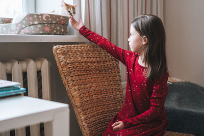 Pretty tween girl with long hair in red dress with cat in children's room at cozy home