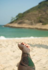 Cropped hand of man showing tattoo at beach