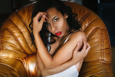 Portrait of sensuous woman lying on brown leather armchair