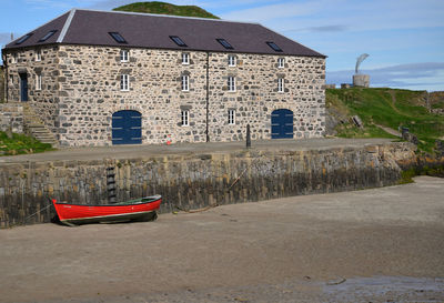 Boat moored on beach by buildings against sky