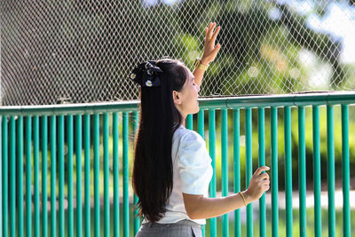 Side view of woman standing against fence