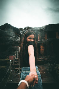 Portrait of woman holding man hand against rock formations and sky