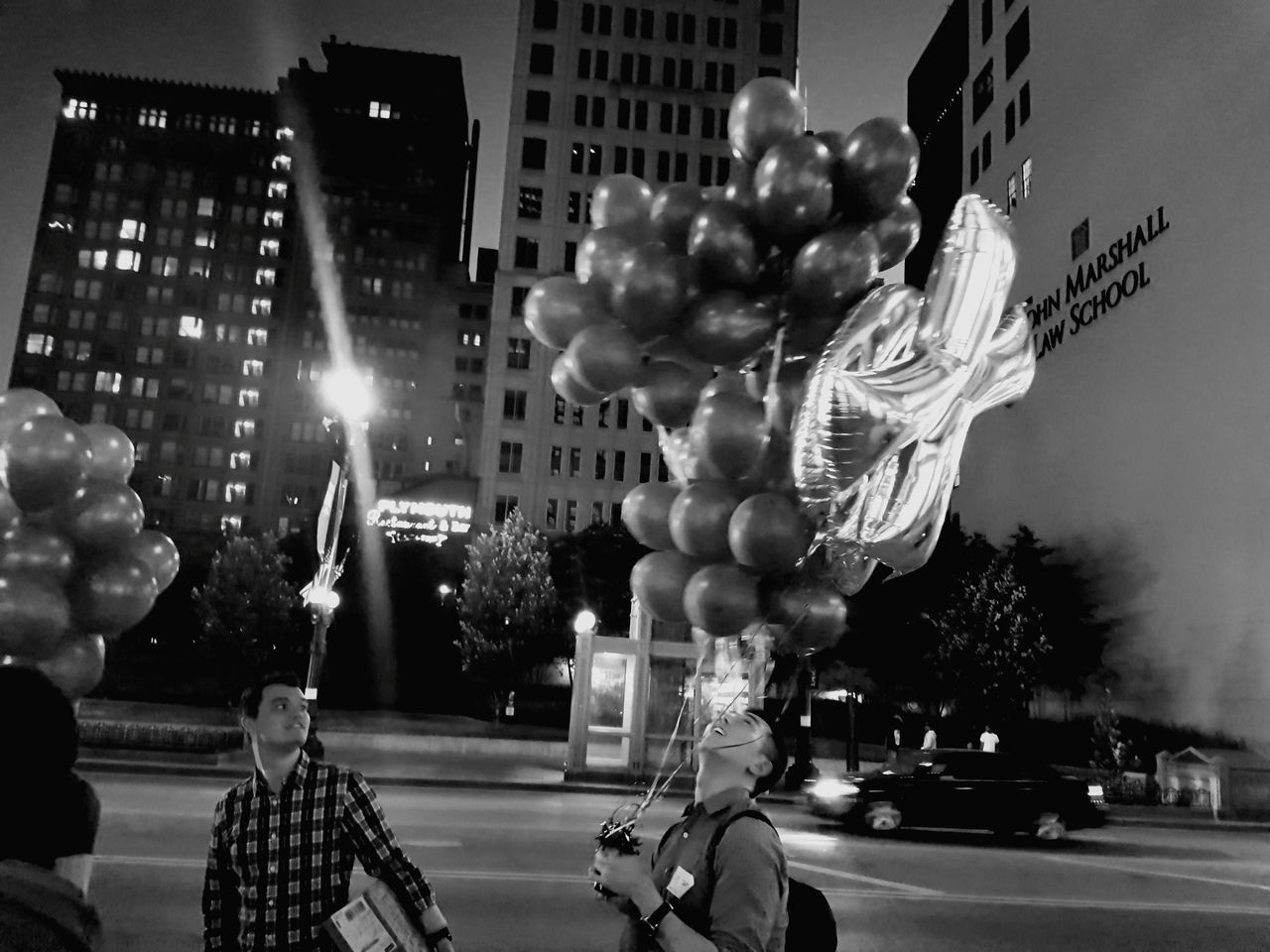 city, street, building exterior, night, architecture, illuminated, built structure, celebration, city life, balloon, outdoors, land vehicle, road, real people, tree