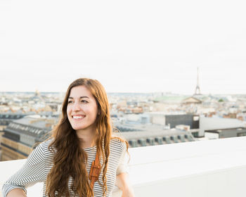 Portrait of smiling young woman in city against sky